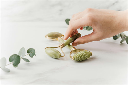 Person using a jade roller on cheek and jawline with serum