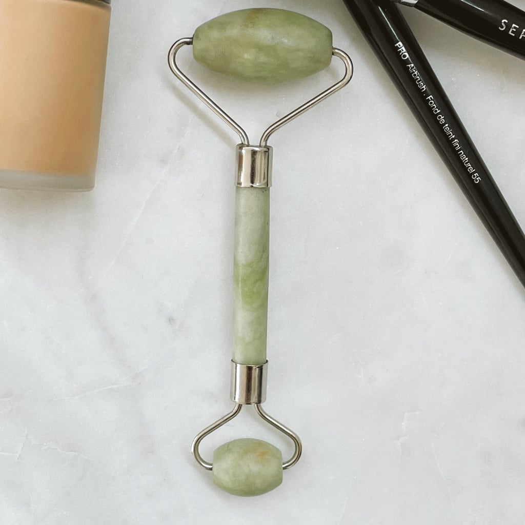 Jade roller in hand on bathroom counter next to phone with TikTok open