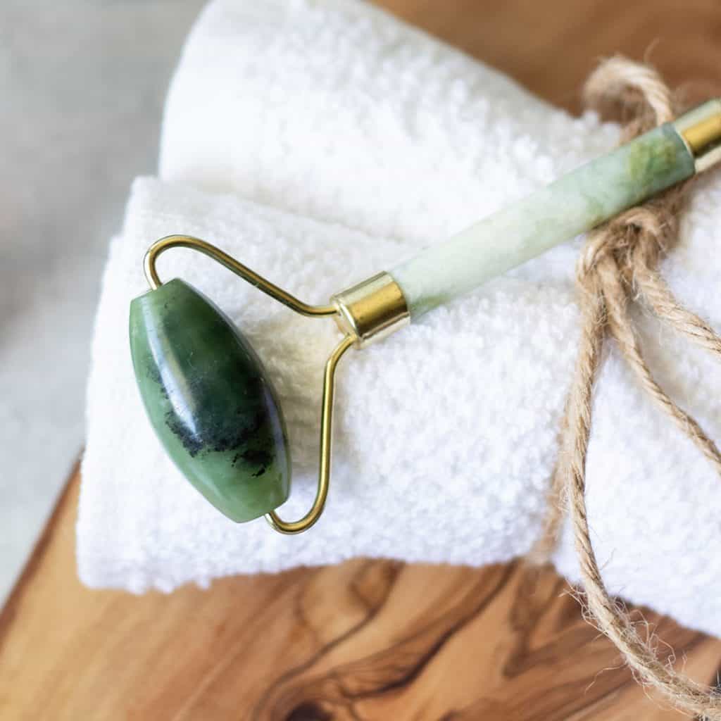 Jade roller being wiped with a soft cloth next to a bowl of soapy water